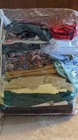 Large clear bag filled with assorted fabric and scraps in various colors and patterns including beige, green, floral, and red pieces.