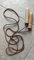 Leather skipping rope with wooden handles shown coiled on tile floor.