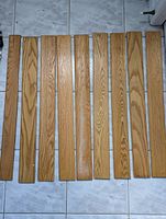 Nine oak wainscotting pieces laid side by side on tiled floor showing natural stain and wood grain pattern.