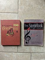 Two old school song books side by side: "The New High Road of Song 5" hardcover and "The Silver Book of Songs" softcover