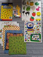 Photo showing mini stickers pack, various themed sticker sheets (animals, fruits, school items), and multiple patterned paper sheets.