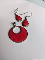 Photo of the red teardrop-shaped earrings and round pendant with a large red inlay, laid on white surface.