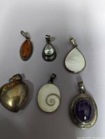 Top view of six pendants arranged on a white background, showing various stone types and silver settings.