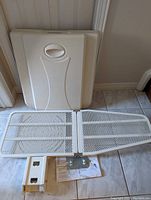 Photo of the ironing board folded out showing the white metal mesh folding surface, plastic mounting cover and mounting bracket with instruction sheet on tile floor.