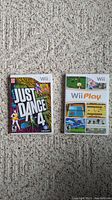 Front covers of Just Dance 4 and Wii Play Nintendo Wii game cases on carpet.