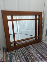 Front angled view showing wooden windowpane style frame and mirror surface with reflection of doorway.