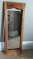 Full view of the wooden framed rectangular mirror standing on floor against wall.
