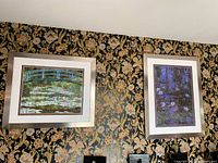 Two framed Claude Monet prints on a floral wallpapered wall, one depicting a Japanese bridge over a pond with water lilies, the other a darker water lily scene.