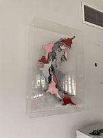 Frontal view of abstract wall sculpture in clear lucite frame showing metallic silver textured elements with pink and red accents.
