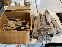 Box of flatware including knives and forks with black handles and gold-tone Thai Buddha decorative tops, along with fabric pouches or wraps.