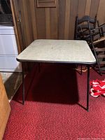 Full view of the square card table standing with all metal folding legs deployed, showing the table top and structure.