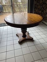Round carved wooden dining table showing full height and base details with gilt wood accents.