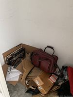 Corner of closet floor showing brown leather bag, Scrabble Classic game box, paper bags and cardboard boxes.