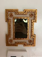 Front view of small rectangular mirror with worn gilt carved floral frame and smudged mirror.