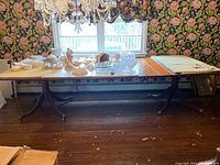 Full view of the wooden dining table set up with leaves and table pads, showing items on top that are not included in the sale.