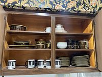 Wooden cabinet interior showing stacked dinner plates, salad plates, cups, bowls