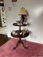Full view of the Georgian style tiered side table with objects including lamp and figurines on it.
