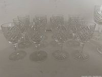 12 extra small and 3 small size cut glass glasses with detailed etched patterns and ornate bases and stems.