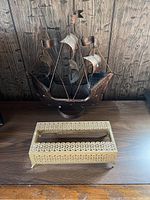 Photo of a decorative metal boat sculpture with sails and a patterned metal tissue box cover on a wood surface.