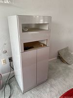 Front view of media cabinet showing two open shelves and closed double door storage below. Some small items and cables visible on middle shelf.