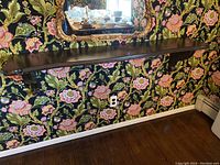 Full view of the carved wooden wall shelf mounted on floral wallpapered wall, showing length and finish.