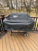 Front view of covered grill on deck with Weber logo visible