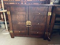 Front view of wooden cabinet showing dark wood finish and gold metal hardware with two doors closed.