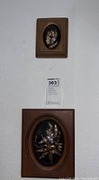 Full view of two frames on white wall, smaller above larger, with catalog tag between them