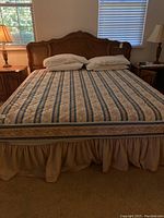 Full view of California King bed setup including wooden headboard, mattress with cover, bed skirt, pillows.