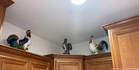 Three ceramic rooster statues displayed on top of cabinets, showing their relative sizes and arrangement.