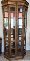 Full front view of hexagonal wooden curio display cabinet with glass doors and shelving inside. Measures 38x18x75 inches.