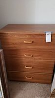 Full frontal view of a wood finish dresser with 4 drawers, showing integrated wood handle pulls and a measuring tag attached.