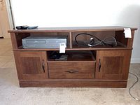 Front view of the wooden media table showing cabinets, drawer, and shelves, with some wear.
