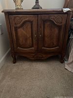 Front view of one wooden nightstand showing carved details on doors, metal handles, and curved legs