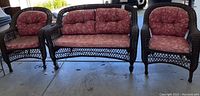 Front view of three-seat settee with two matching chairs in dark brown wicker with red floral cushions.