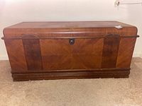 Front view of wooden cedar chest showing wood veneer finish, combo lock, and carved decorative accents.