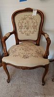 Full view of vintage wooden chair with curved arms and carved frame, upholstered with floral needlepoint fabric.