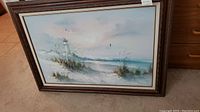 Full front view of the framed oil painting showing the lighthouse seascape scene, seagulls, waves and coastal plants.