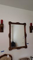 Wall mirror with ornate carved wood frame flanked by two candle votive shelves holding red candles, set against white wall