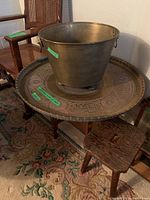Overall image showing brass bucket placed on engraved brass platter atop a wood and brass stand with a wooden stool adjacent.