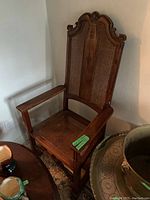 Full view of an antique hardwood bishop's chair with decorative carved crest and caned seat and back placed in room corner.