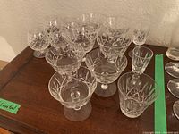 Photo showing the full set of 14 clear crystal stemware glasses with etched cross and olive pattern arranged on a wooden surface.