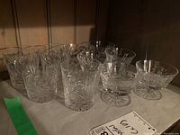 Set of 10 crystal glasses in pinwheel pattern showing both tumblers and stemmed glasses grouped together on shelf.