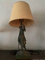 Full view of the lamp showing the figurine and beige shade.