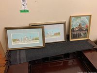 Three framed paintings by J. H. J. Dix displayed on a table against a wall: two horizontal paintings of the Taj Mahal and one vertical painting of a temple.