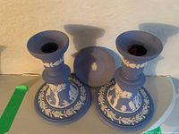 Front and top view of 2 Wedgwood blue jasperware candle holders and a miniature plate with white classical relief decorations.