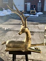 Front three-quarter view of brass stag deer sculpture on wooden stand, showing overall form and proportions.