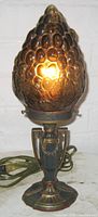 Front view of the lit amber grape glass lamp showing detailed texture and colors of shade and ornate metal base.