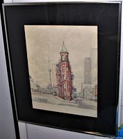 Angle view of framed watercolour painting depicting Toronto's Flatiron Building with city skyline including CN Tower, framed in silver frame with black mat.