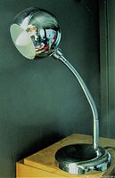 Front view of chrome spherical desk lamp with flexible gooseneck and circular base on wooden surface against black background